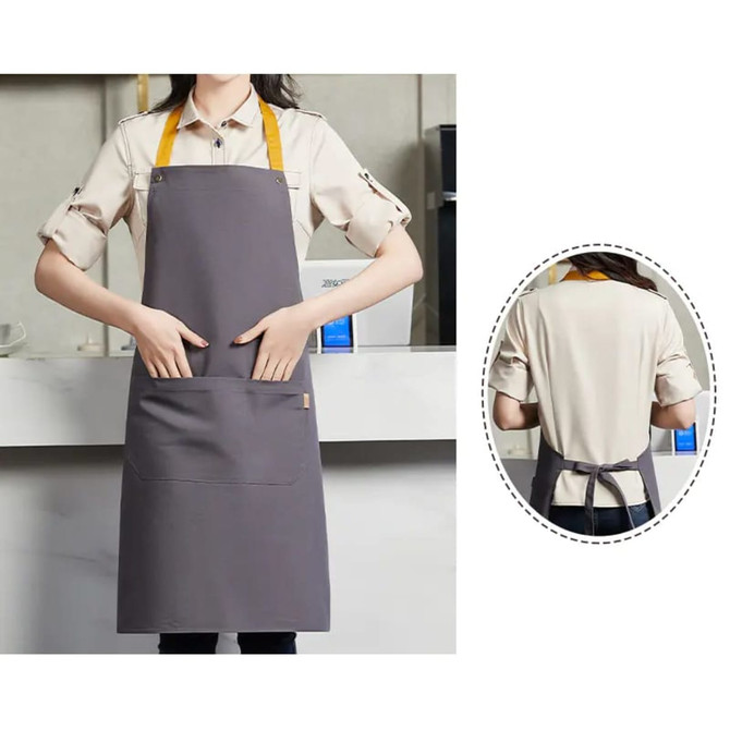 A grey poly-cotton canvas bib apron with a yellow neck strap and front pocket, featuring a branding logo.