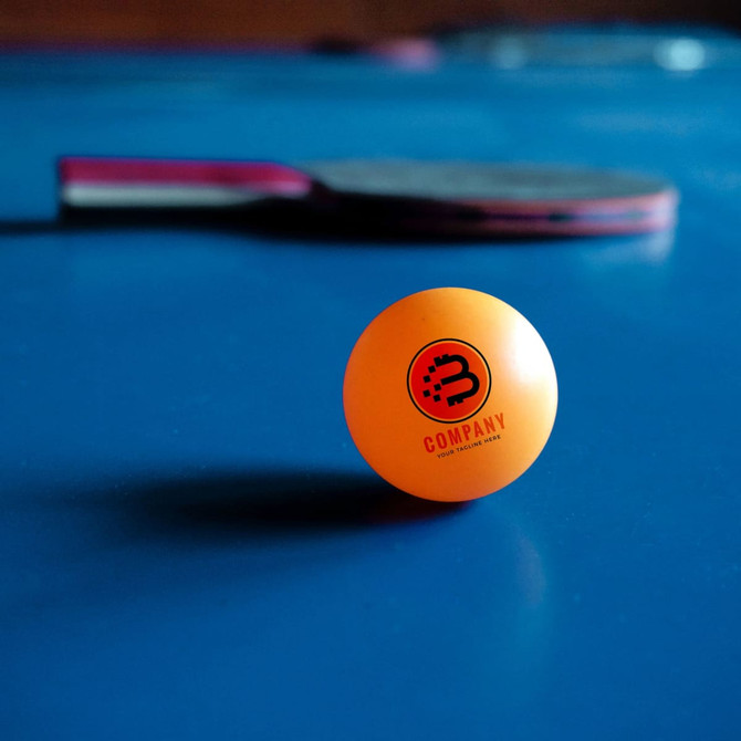 A set of six orange table tennis balls with a logo, placed on a blue table surface alongside a paddle.