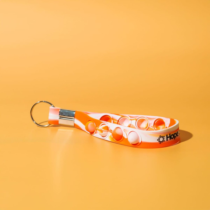 An orange and white stress reliever key chain featuring poppable buttons and a metal keyring.