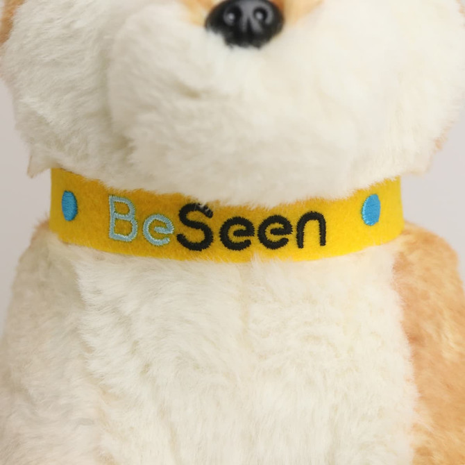 A custom plush dingo toy with a soft, tan and white fur coat and a bright yellow collar featuring embroidered text.