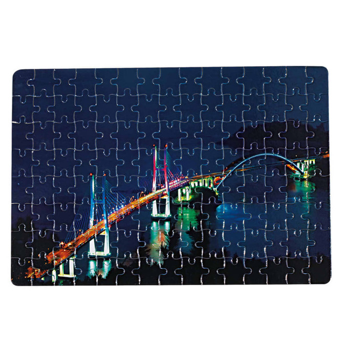 A jigsaw puzzle featuring a brightly lit bridge at night, with various blue and green tones. It has a logo on the corner.