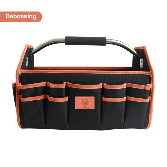 A black tool carrier bag with orange accents, featuring multiple pockets and a metal handle. It has a logo on it.