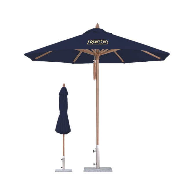 A navy blue outdoor umbrella with a wooden pole and base, featuring a logo. Another folded umbrella is beside it.
