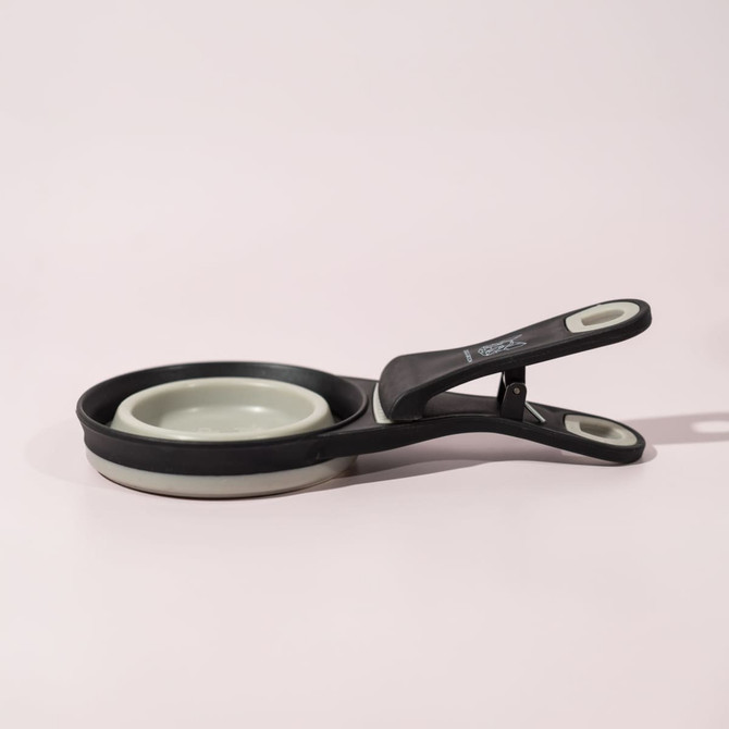 A collapsible silicone pet food scoop and bag clip in black and grey, featuring a sleek design and a logo.