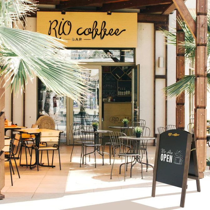 A-frame chalkboard in black displaying an open sign, set outside a café with wooden beams and greenery.