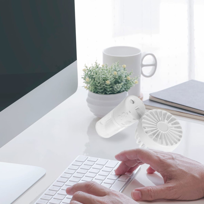 A clear neck spray fan sits next to a computer, surrounded by a plant and mug on a desk.