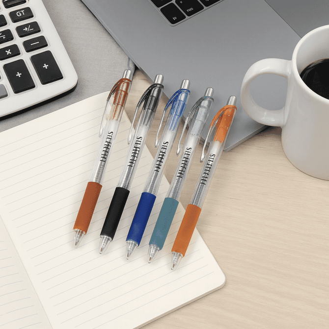 A set of five colourful gel ink pens in black, blue, orange, and teal, positioned on a notepad next to a laptop and coffee cup.