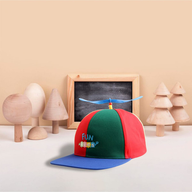 A red, green, and blue Propeller Baseball Cap with a logo, set against a backdrop of wooden toys and a chalkboard.