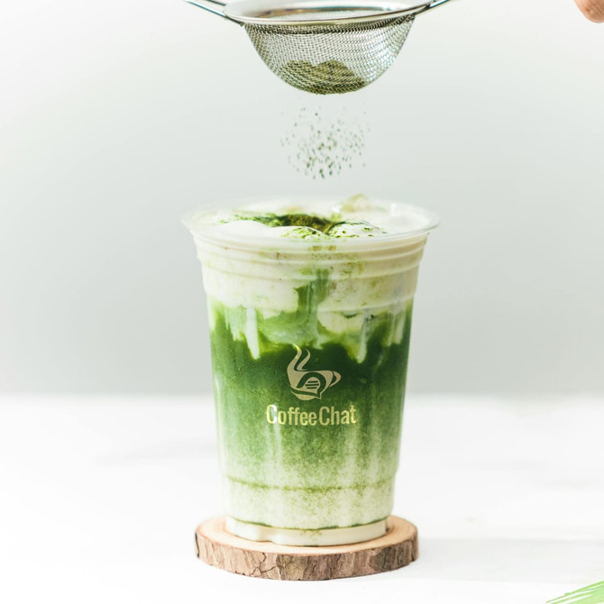 A clear plastic cup filled with a green drink and topped with frothy cream, featuring a logo on the cup. A clear plastic cup filled with a green drink and topped with frothy cream, featuring a logo on the cup.