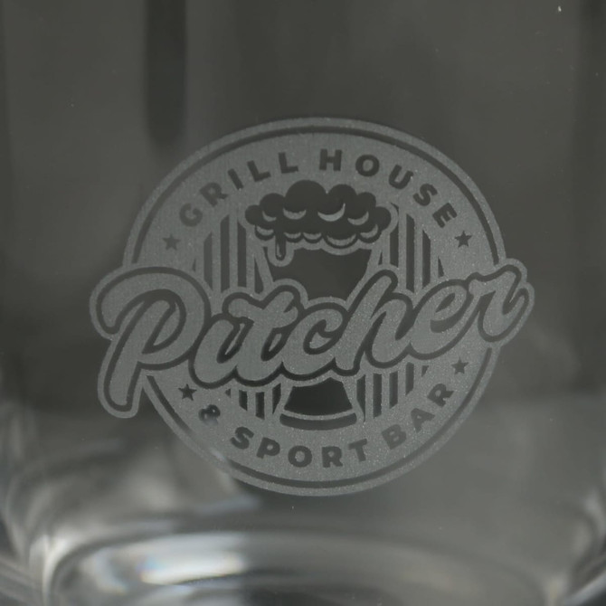 A clear glass cup featuring an engraved logo. The design includes elements related to a grill house and sports bar.