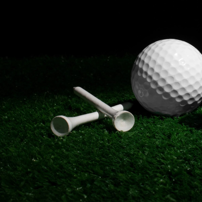 A bamboo golf tee in white, positioned next to a golf ball on green grass.