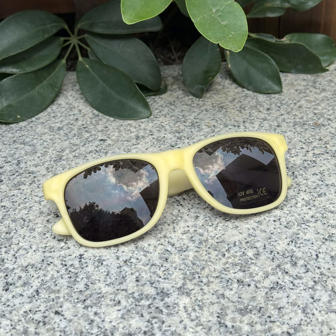 Colour changing sunglasses in a soft yellow frame resting on a stone surface, surrounded by green foliage.