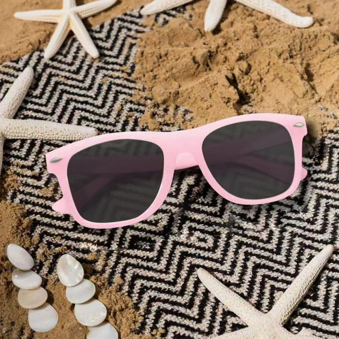 A pair of pink glow-in-the-dark sunglasses resting on a sandy surface, surrounded by starfish and seashells.