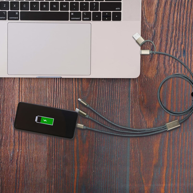A black capsule storage charging cable with three connectors rests next to a silver laptop on a wooden surface.