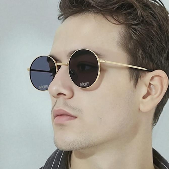 Retro round sunglasses with a black lens and gold frame, featuring a logo on the side.