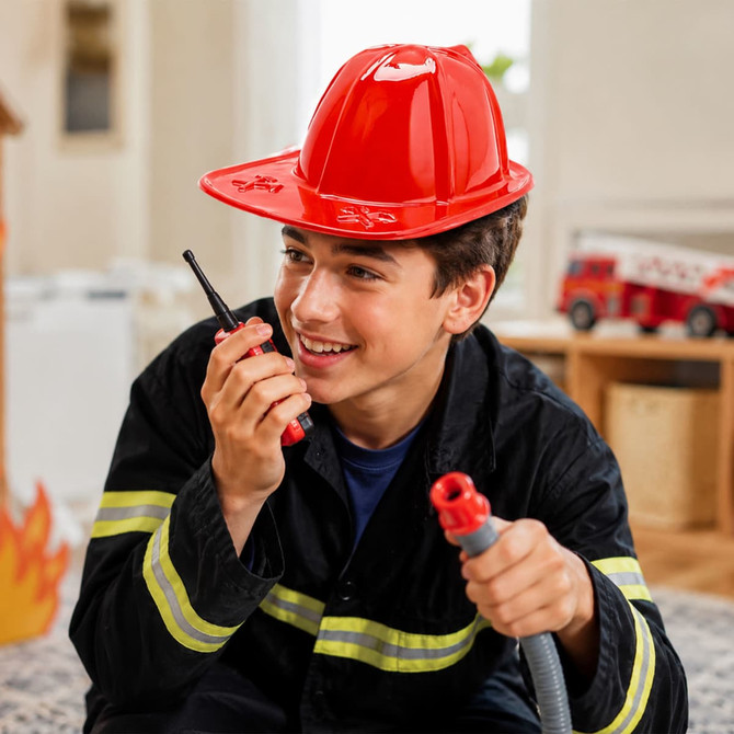 A bright red PVC fire chief hat is worn by a boy holding a walkie-talkie, dressed in a firefighter costume.