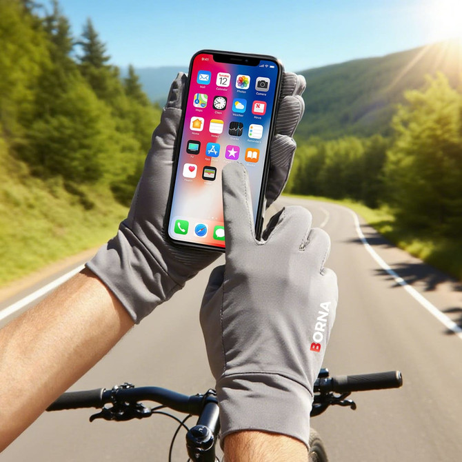 A pair of grey touchscreen gloves is shown, with a hand using a smartphone outdoors near a bike trail.