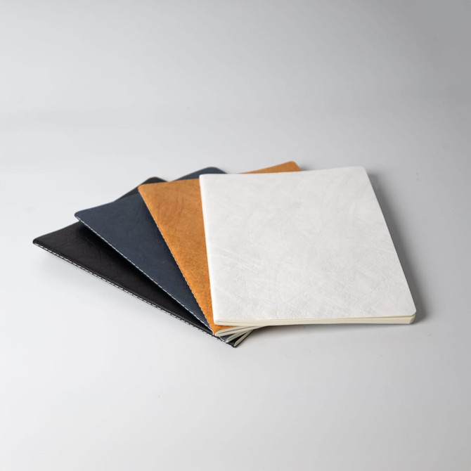A set of four notebooks in black, navy, brown, and white, featuring smooth covers and a clean design.