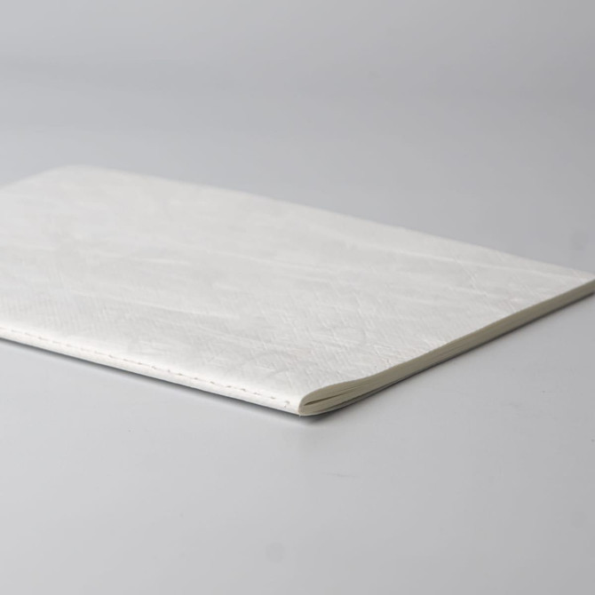 A white notebook with a textured cover lying flat on a grey surface. It features a subtle seam along one edge.