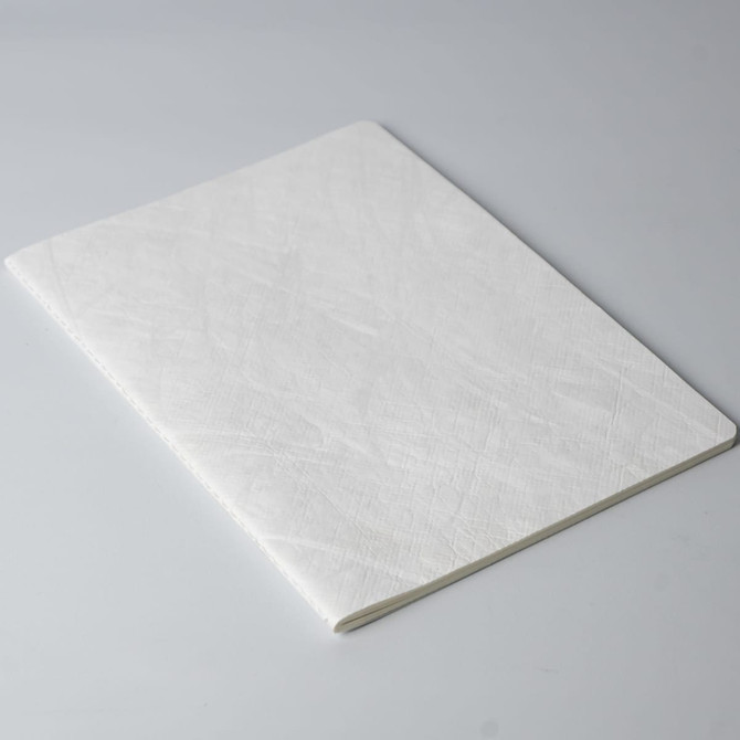 A white notebook with a smooth cover, lying flat on a grey surface. It has no visible branding.