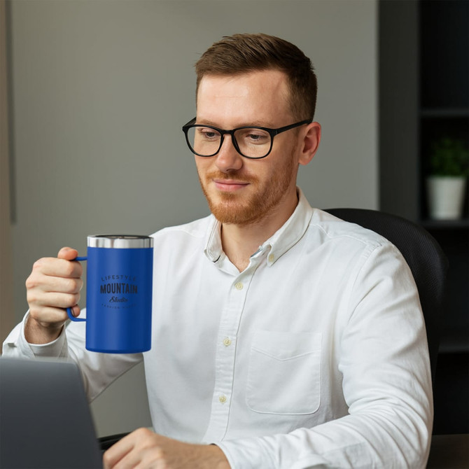 A blue stainless steel mug with a handle sits in the hand of a man wearing glasses, at a desk with a laptop. A blue stainless steel mug with a handle sits in the hand of a man wearing glasses, at a desk with a laptop.