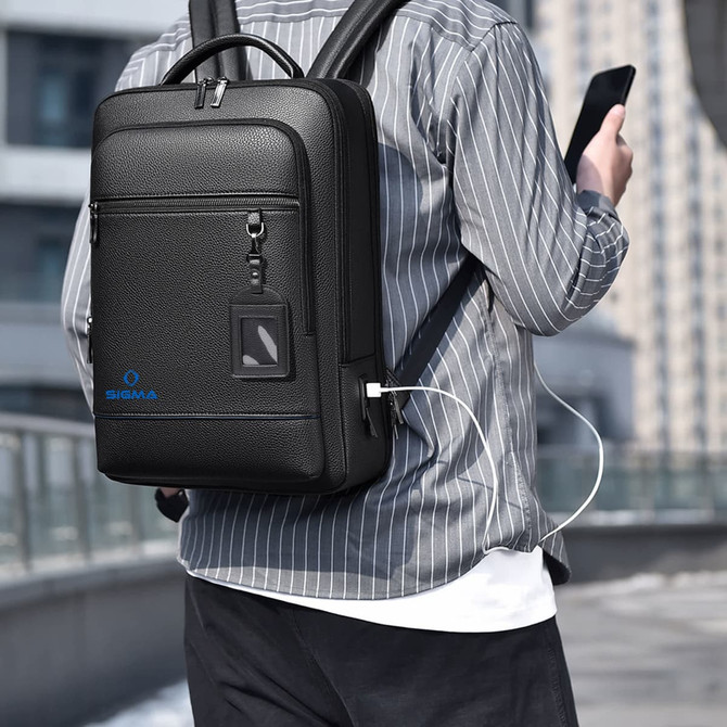 A black polyurethane laptop backpack with a USB charging port, worn on a person's back in a city setting.