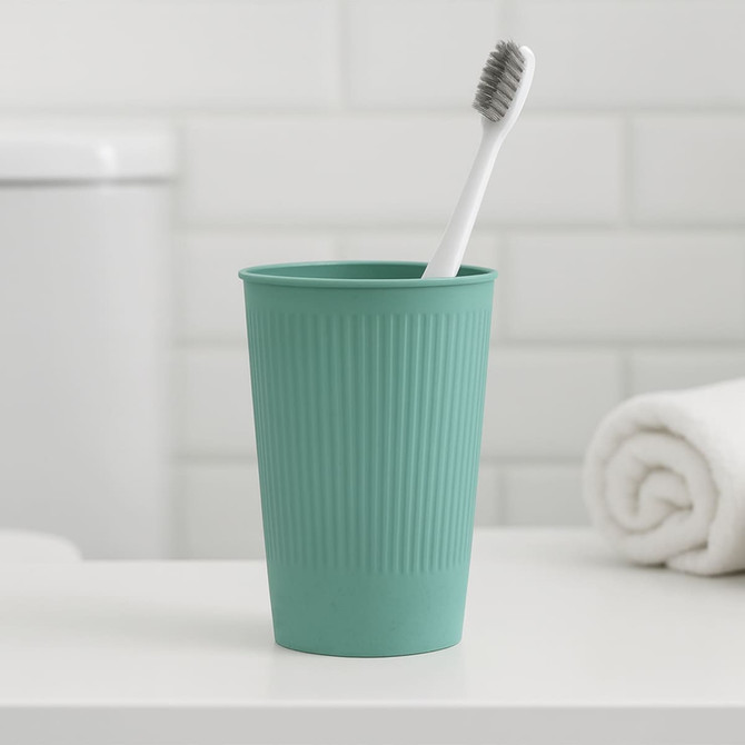 A teal wheat straw toothbrush cup with ridged texture, containing a white toothbrush, set on a bathroom counter. A teal wheat straw toothbrush cup with ridged texture, containing a white toothbrush, set on a bathroom counter.
