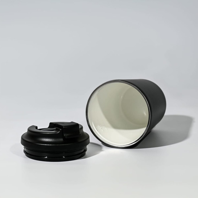 A travel cup in black with a removable lid, featuring a stainless steel inner lining and a sleek design.