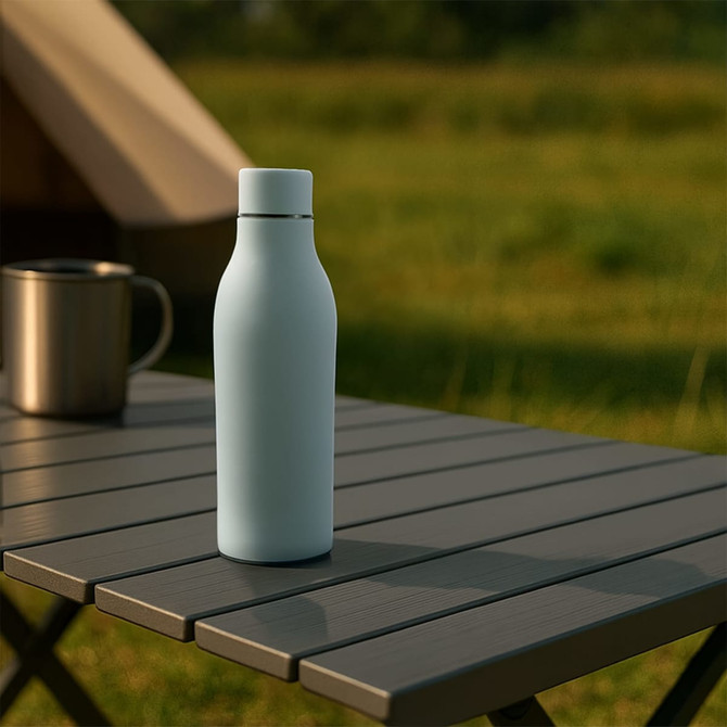 A drink bottle with a rubber-coated light blue exterior sits on a table in a natural setting. It features a logo.