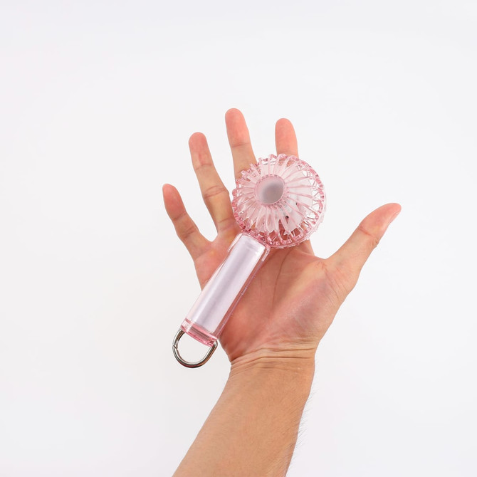 A pink transparent fan with LED light is held in a hand, featuring a handle and a round fan blade design.