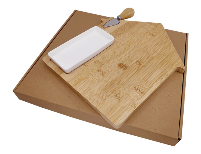 A bamboo cheese board in the shape of a house, featuring a ceramic dish and a knife, packaged in a brown cardboard box.