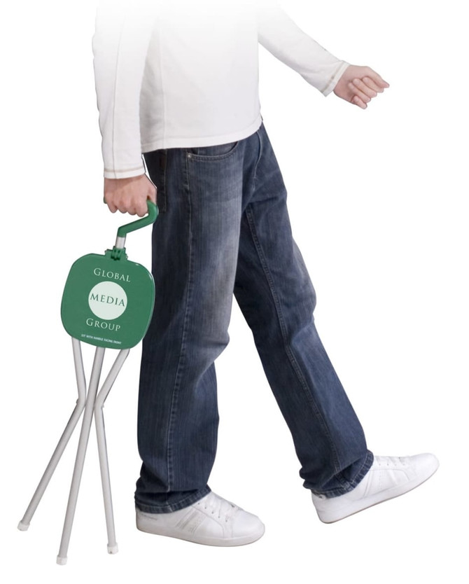 A green folding chair being carried by a person in jeans and white shoes, featuring a logo on the backrest.