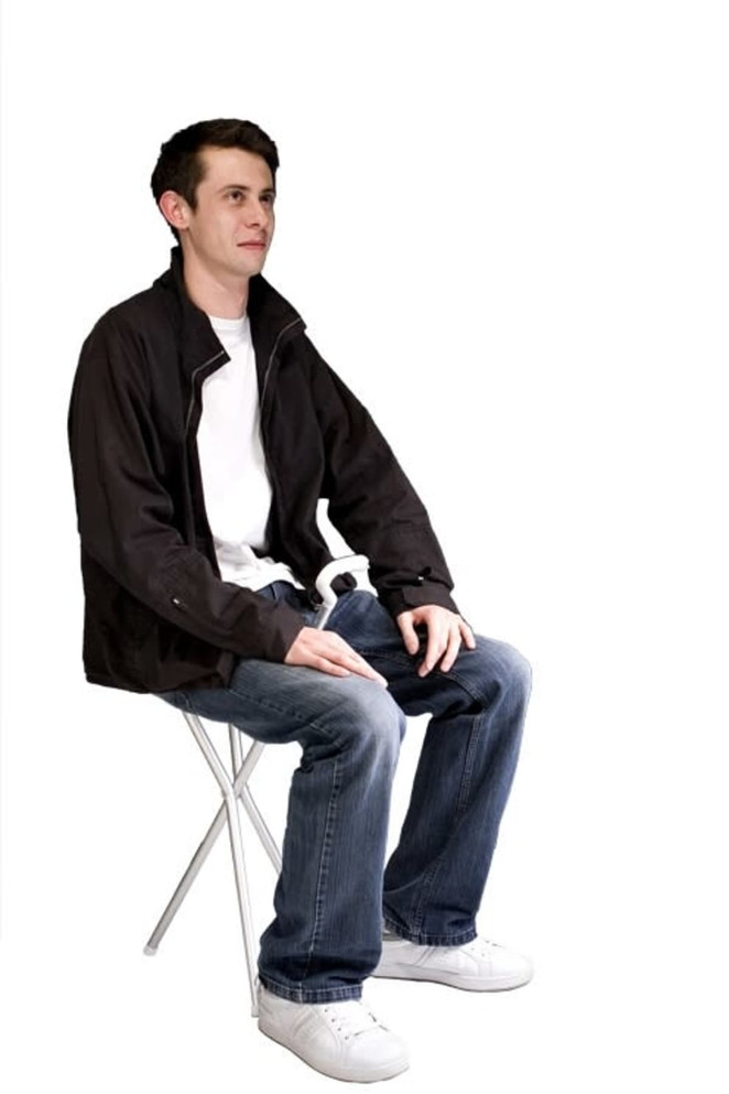 A compact folding chair in white with a person seated, wearing casual attire and a black jacket.