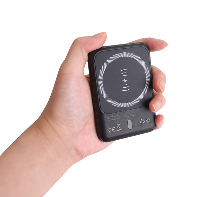 A black 5000mAh eco magnetic power bank held in a hand, featuring a circular design on the surface.