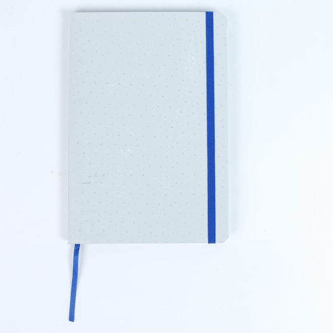 A grey notebook with a blue elastic band and ribbon marker, featuring a dotted texture on the cover.