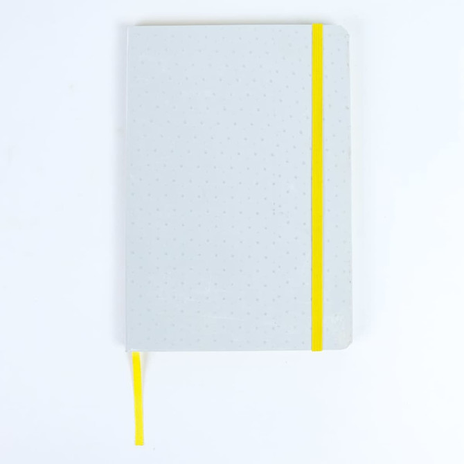 A grey notebook with a yellow elastic band and ribbon bookmark. It features a dotted interior design.