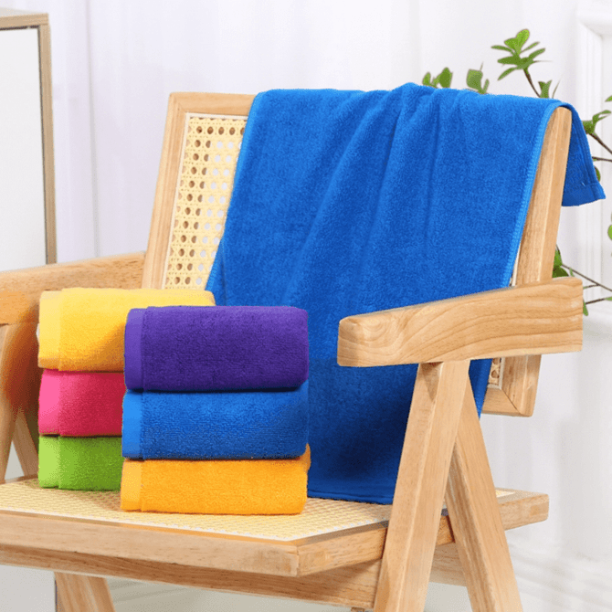 A stack of vibrant gym towels in purple, pink, blue, and orange, placed on a wooden chair with a larger blue towel draped on the back. A stack of vibrant gym towels in purple, pink, blue, and orange, placed on a wooden chair with a larger blue towel draped on the back.