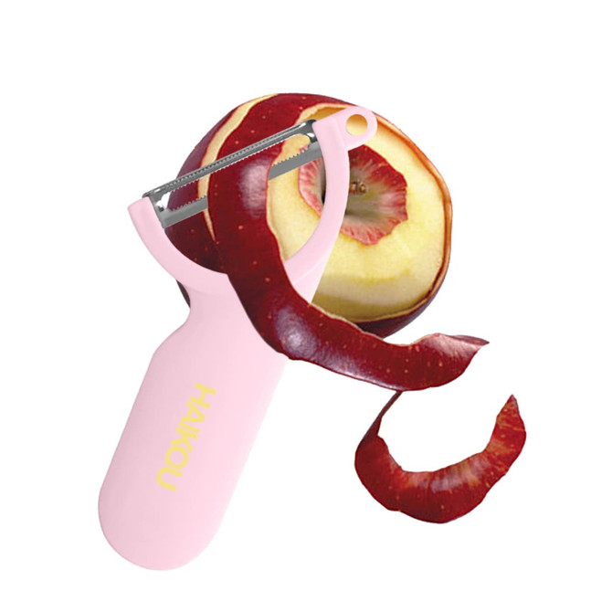 A pink vegetable peeler with a metal blade, alongside a partially peeled red apple and a long strip of apple skin.