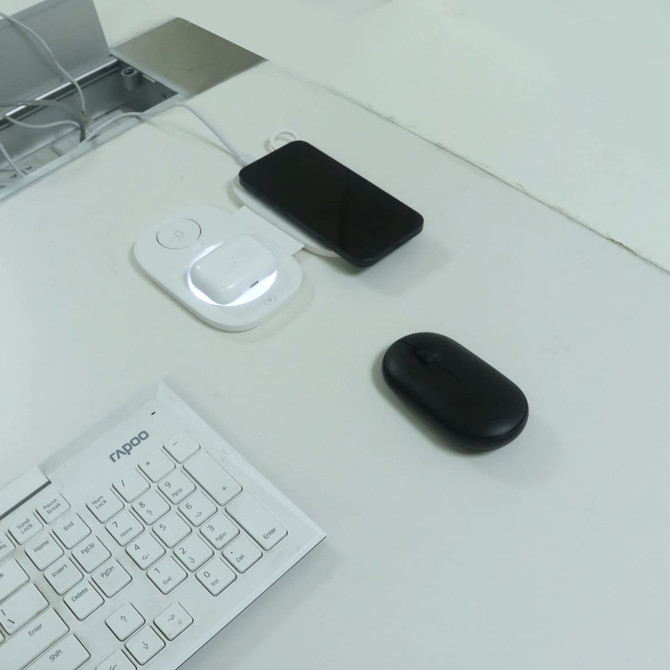 A black mouse and a smartphone charging on a white 3-in-1 wireless travel charger on a desk.
