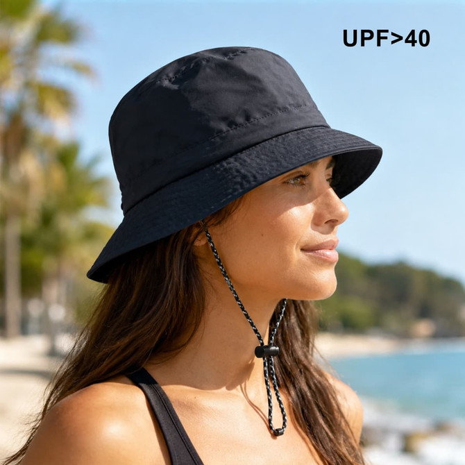 A foldable black bucket hat with a chin strap and a logo, set against a beach background.