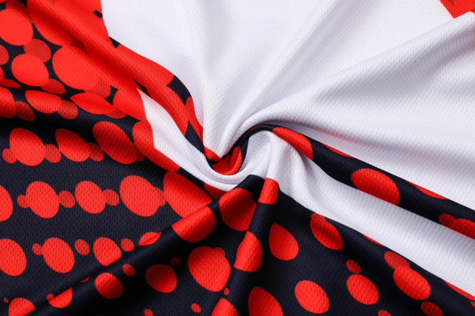 A close-up of a sublimated football jersey featuring a red, white, and black design with circular patterns and a logo.