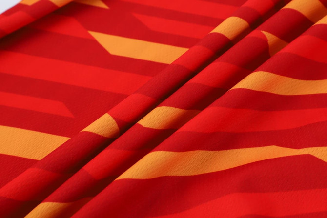 A close-up of a vibrant red micro mesh fabric featuring bold yellow and orange geometric patterns, with a soft texture.