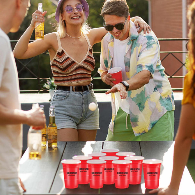 A set of red party cups arranged for beer pong, with people enjoying drinks and playing in a lively outdoor setting.