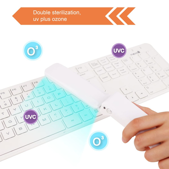A portable UV steriliser in white is held over a white keyboard, emitting blue light for disinfection.