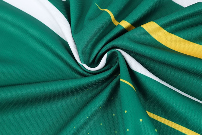 A green and white sports tee shirt with a swirling pattern and yellow accents, featuring a logo.