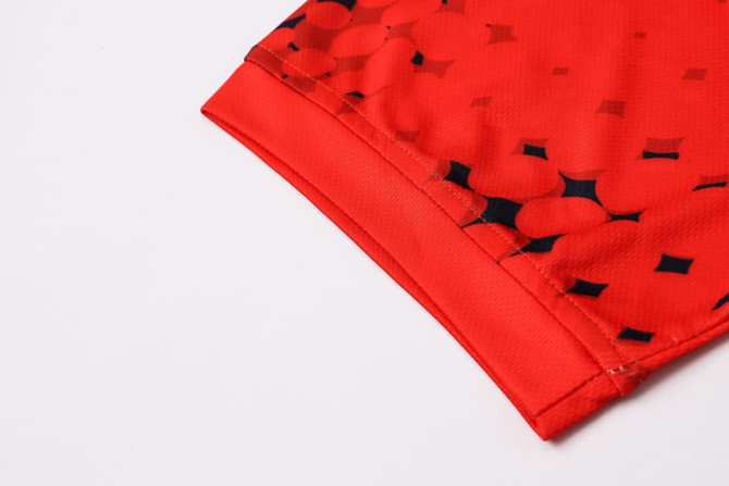 A close-up of a red football jersey featuring a patterned design, made from 100% polyester with a logo.
