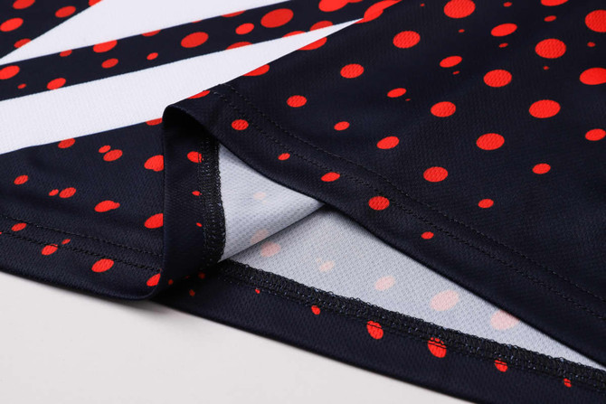 A close-up of a unisex football jersey featuring a navy background with red polka dots and white accents.
