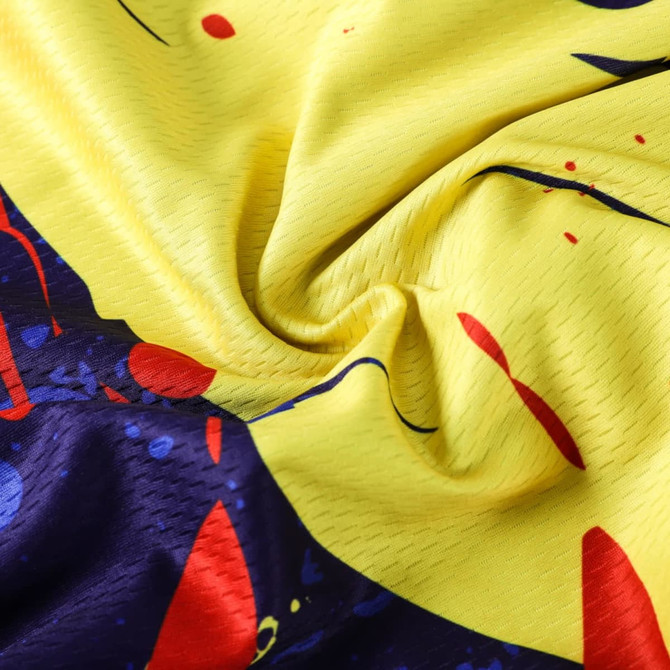 A close-up of a yellow and navy sublimated fabric featuring vibrant splashes of red and blue, typical for a cycling jersey.