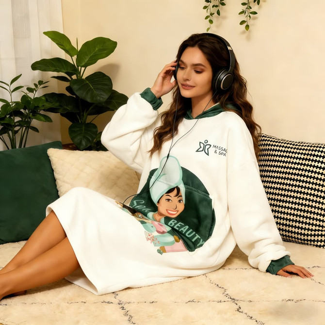 A wearable blanket in white with a green hood, featuring an illustrated design and branding.