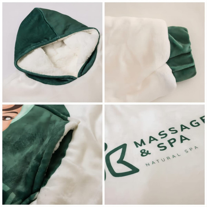 A wearable blanket in white and green, featuring a hood and soft lining, with a logo on the front.
